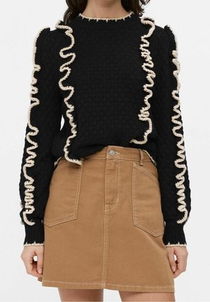 Femme portant un pull noir texturé avec un bord volanté crème et une jupe marron taille haute en ligne A avec poches plaquées à l'avant.