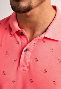 Rosa polo skjorta med små svarta flamingomönster, med en texturerad tyg, klassisk krage, tvåknapps knäppning och en diskret logotyp på knappen.