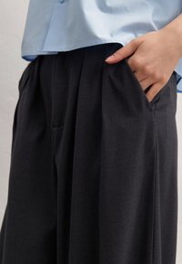Dark gray wide-leg trousers with sharp pleats and side pockets, made from a smooth fabric, paired with a light blue collared shirt.