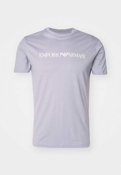 Heleda lilla puuvillane T-särk, millel on ümar kaelus ja lühikesed varrukad, ning rinna peal on valge kiri "EMPORIO ARMANI".