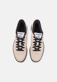 Baskets en daim fauve avec lacets et doublure intérieure noirs. Devant perforé, semelle en caoutchouc et étiquette logo Reebok Classic blanche.