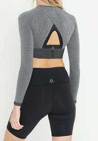 Graues, langärmliges Sportoberteil mit einem dreieckigen Ausschnitt am Rücken, kombiniert mit hochtaillierten schwarzen Shorts, die ein dezentes Logo tragen.