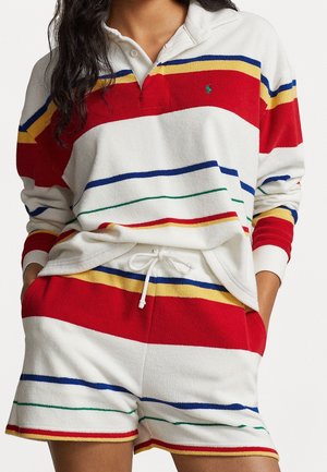 Persona vistiendo un conjunto de pantalón corto y parte superior de felpa blanca con rayas horizontales en rojo, amarillo, azul y verde, incluyendo una camiseta de manga larga y pantalones cortos con cordón.