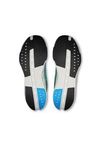 Des chaussures de sport avec une semelle en caoutchouc noir texturé, une intermédiaire blanche et des accents bleus. La tige présente un motif vert.