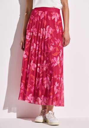 Faltenrock in leuchtendem Pink mit floralen Mustern in hellerem Pink und Orange. Weiches, leichtes Gewebe; elastischer Bund. Kombiniert mit weißen Sneakers.