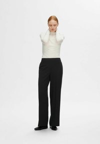 Schwarze hochgeschnittene Hosen mit geradem Schnitt, aus glattem Stoff, kombiniert mit einem weißen Langarm-Turtleneck-Oberteil.