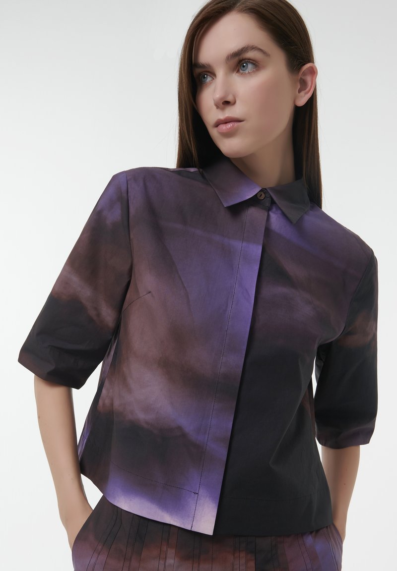 Short-sleeved shirt in blended purple and black fabric, featuring a pointed collar and a button closure, with a smooth texture and modern cut.