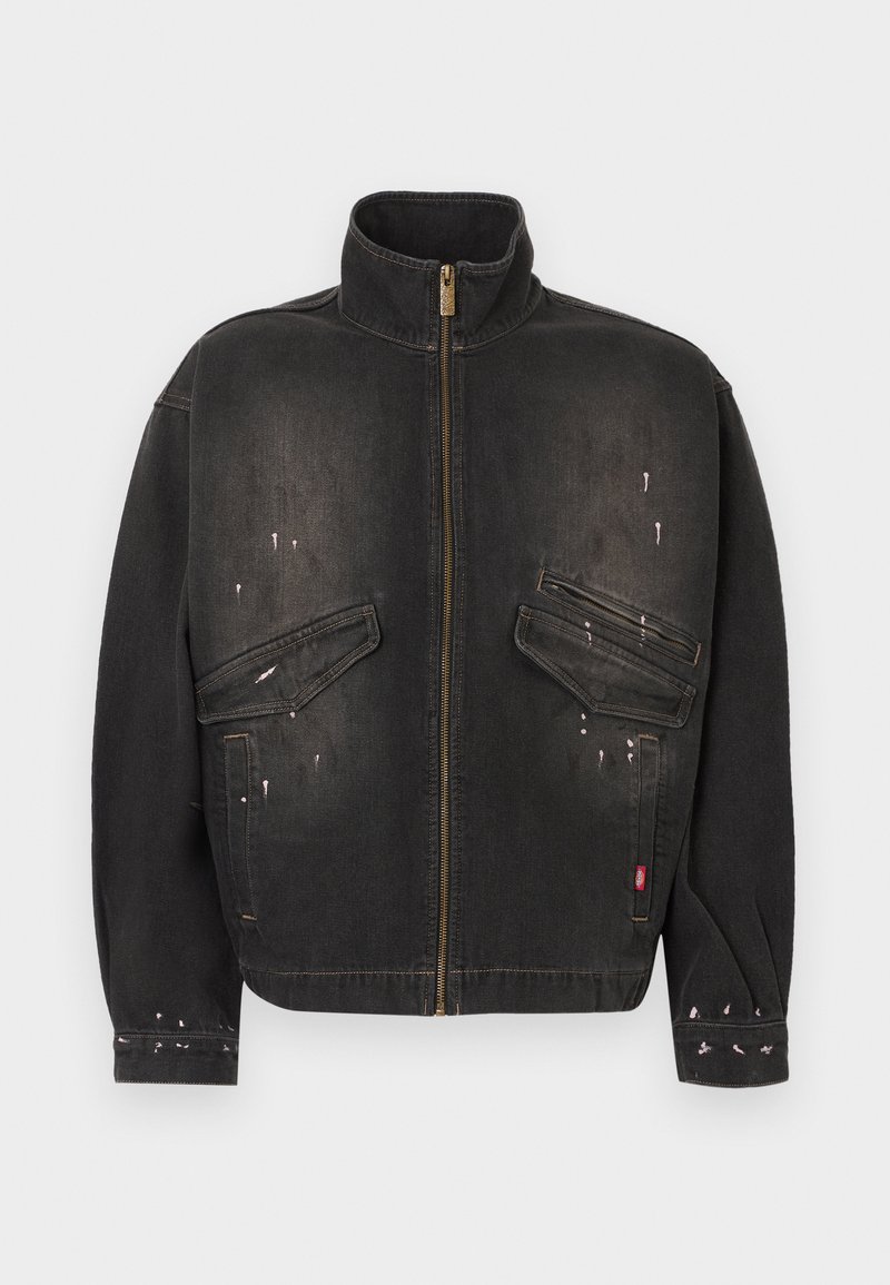 Giacca in denim nero sbiadito con collo alto, zip frontale, due tasche con patta inclinate e lievi schizzi di vernice sul davanti e sulle maniche.