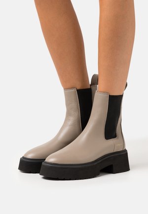 Beige leather ankle boots with black elastic side panels, rounded toes, and chunky black rubber soles. Simple design with minimal hardware.
