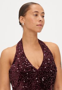 Vestido de tirantes burdeos con lentejuelas que presenta un escote en V profundo y una silueta ajustada, resaltado por lentejuelas brillantes y reflectantes en toda su superficie.