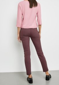 Pantaloni aderenti con un motivo geometrico rosso su uno sfondo scuro, abbinati a una maglietta rosa a maniche corte. Scarpe nere basse completano l'outfit.