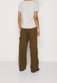 Grijs katoenen T-shirt gecombineerd met olijfgroene cargobroeken met brede pijpen. De broek heeft grote zijzakken en omgeslagen boorden. Zwart schoeisel zichtbaar.