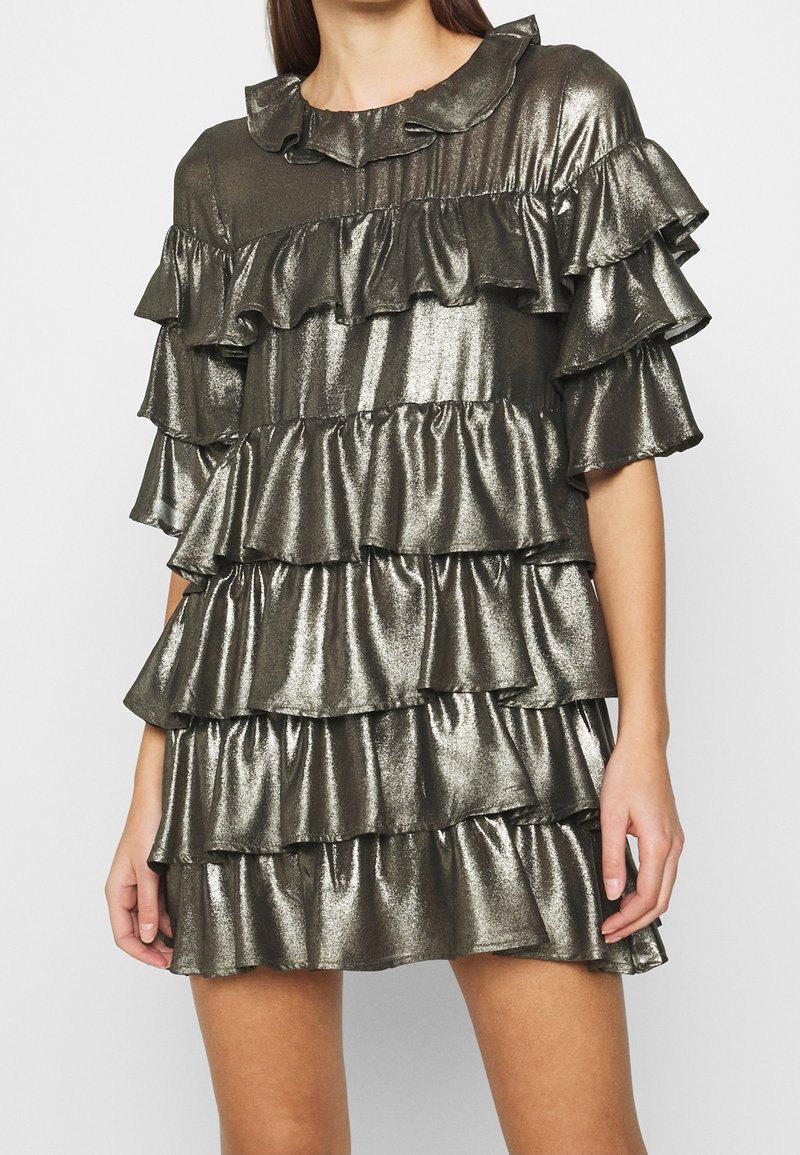 Puku metallinen kiiltävä mekko, jossa on useita röyhelökerroksia, lyhyet hihat ja pyöreä pääntie. Väri on tumma hopea ja pinta on sileä.