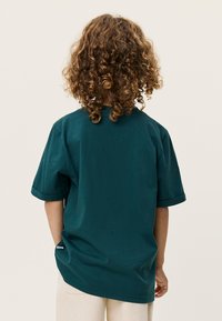 Τζίνελ μπλουζάκι από βαμβάκι με κοντά μανίκια, γυρισμένα τελειώματα και άνετη εφαρμογή. Η πίσω όψη δείχνει ομαλή υφή και ελάχιστη σήμανση στο κάτω μέρος.