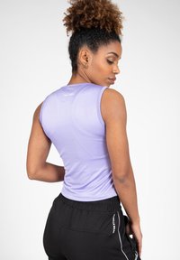 Paarse mouwloze sporttop met een aansluitend ontwerp en een gladde textuur, gecombineerd met zwarte broek met drawstring en witte accenten.