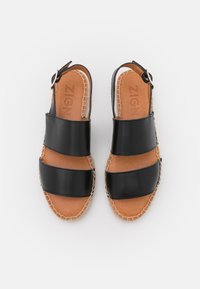 Sandali neri in pelle con due larga cinghie e fibbia alla caviglia, soletta imbottita color tan e suola leggera cucita su uno sfondo bianco.