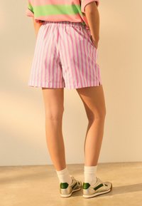 Różowo-białe szorty w paski z elastycznym pasem, prezentowane na jasnym tle, ukazujące swobodny, luźny krój.