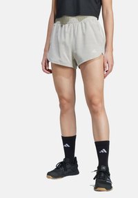 Světle šedé sportovní šortky s elastickým pasem, se bočními rozparky, doplněné černými sportovními ponožkami a černými botami.