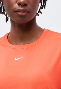 Nahaufnahme einer Person, die ein leuchtend oranges Nike-Sportshirt trägt, auf dem das weiße Swoosh-Logo auf der Brust sichtbar ist.