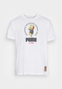 Camiseta blanca de algodón con un oso de dibujos animados vestido con un traje negro, texto en un logo redondo "GOLDBEAR SPORTING GOODS CLUB" y "PUMA HARIBO". Parche distintivo en el dobladillo.