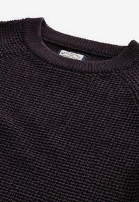 Dunkellila gestrickter Pullover mit geripptem Rundhalsausschnitt und strukturiertem Muster, mit einem Etikett in der Nähe des Ausschnitts.