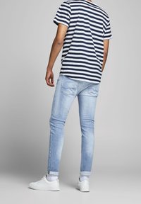 Randig marinblå och vit t-shirt, ljusblå denimjeans med slim fit, och vita sneakers, visar en avslappnad outfit från baksidan.