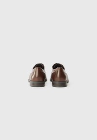 Chaussures en cuir marron avec une finition lisse, bout arrondi et petit talon. L'arrière présente une texture subtile et un détail de couture près de l'ouverture.