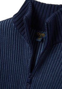 Dunkelblauer Kinder-Reißverschluss-Pullover mit geripptem Textur, hohem Kragen und kontrastierenden helleren Streifen; ausgestattet mit einem Reißverschluss und Etikett.