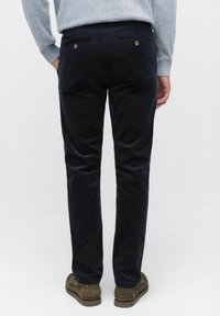 Marinblå kordfläktbyxor med rak ben, två bakfickor, silverknappar och en slät yta. Bärs med bruna loafers.