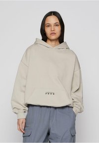 Beež kapuutsiga pusa, millel on esiosas tasku ja must tekst "PEGADOR PGDR" taskul. Riie tundub pehme ning lõdvestunud, üle mõõdu suures istuvuses.