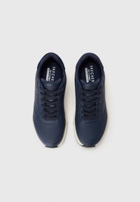 Navy blue Skechers athletic shoes with perforated design, flat laces, and a white sole. Soft material and padded interior for comfort.