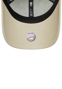 Gorra de béisbol beige con visera negra, con una pegatina circular que se asemeja a una pelota de béisbol en la parte inferior. Tejido texturizado con detalles de costura.