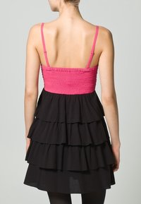 Robe noire à volants avec un corsage smocké rose et des bretelles ajustables. La jupe présente plusieurs couches froncées pour une texture supplémentaire.