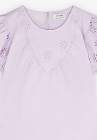 Lila Bluse mit besticktem Blumenmuster, gewelltem Ausschnitt und Puffärmeln. Weicher Stoff mit gerafftem Detail an der Taille.