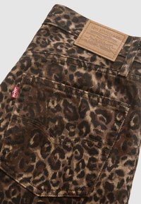 Denim hlače Levi's z rjavim leopardjim potiskom, usnjenim žepnim ojačitvenim delom z blagovno znamko in rdečo tablico na strani zadnjega žepa.
