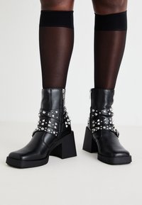 Black ankle boots with a chunky heel, featuring silver studs and straps, made of leather with a smooth texture and a zip closure.