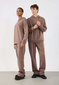 Brązowe, dopasowane bluzy z kapturem i spodnie dresowe z miękkiej, teksturowanej tkaniny. Luźny krój z ściągaczami na rękawach i u dołu, zestawione z czarnymi butami.