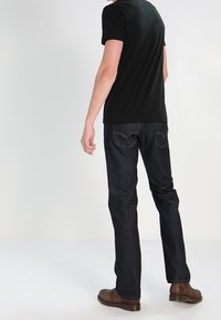 Černé tričko s krátkým rukávem v kombinaci s tmavě modrými džíny. Slim-fit design s zadními kapsami a minimálním detailem šití. Hnědé boty.