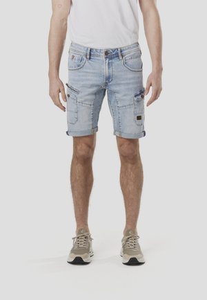 Jasnoniebieskie jeansowe szorty z wieloma kieszeniami, podwiniętymi mankietami i wyblakłym wykończeniem, noszone z beżowymi sneakersami. Gładka tekstura i casualowy design.