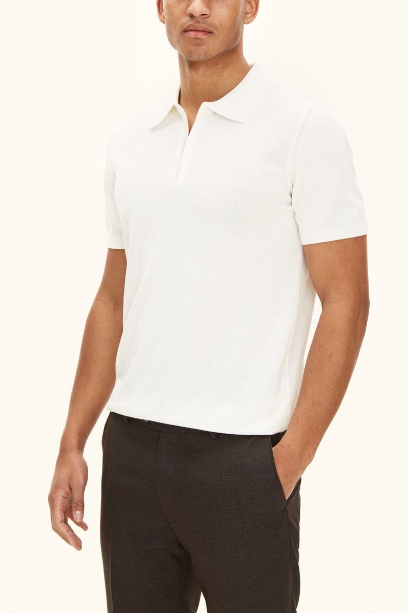 Valkoinen, lyhythihainen poolopaita, jossa on kaulus ja puolipitkä napitus, teksturoitua kangasta, yhdistettynä tummiin räätälöityihin housuihin.