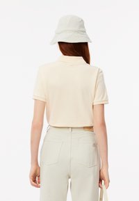 Lichtbeige poloshirt met korte mouwen, van een gestructureerde stof. Gecombineerd met lichte broek en een zachte, lichtgrijze bucket hat.