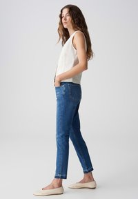 Top sans manches ivoire, jeans bleus slim-fit et chaussures beige à enfiler. Tissu lisse, design simple et détails de couture subtils.