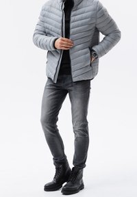 Szara kurtka puchowa z pionowymi przeszyciami, czarny sweter o fakturze, szare jeansy oraz czarne wiązane buty na masywnych podeszwach. Na nadgarstkach zegarki.