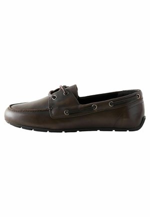 Scarpa da barca in pelle marrone con punta arrotondata, lacci a contrasto e occhielli in metallo. La suola è nera e testurizzata per una migliore aderenza.