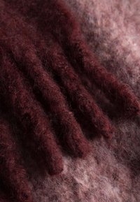 Bordeaux wollen wanten met getextureerde, verlengde vingers op een zachte, roze achtergrond, met een fuzzy afwerking en gelaagde vezels.