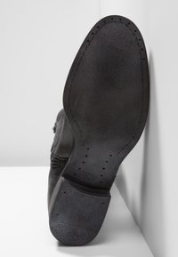 Semelle de botte en cuir noir avec une prise en caoutchouc texturée, forme arrondie et surpiqûres sur le bord ; présente de petits trous et une surface lisse.