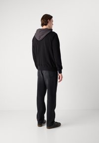 Felpa nera con cappuccio grigio, polsini e orlo a costine. Abbinata a jeans grigi scuri a vestibilità ampia e scarpe nere. Vista da dietro.