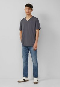 Szary t-shirt z dekoltem w serek, krótki rękaw, w zestawie z jasnoniebieskimi dżinsami i białymi sneakersami z brązowymi akcentami. Prosty, casualowy wygląd.