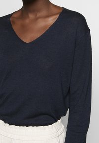 Granatowy, lekki sweter dziany z dekoltem w serek, długimi rękawami i fakturowaną tkaniną, zestawiony z kremowym, prążkowanym dołem z zaznaczoną talią.