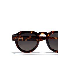 Gafas de sol de carey marrón con lentes redondos, una barra ancha en el ceño y el nombre de la marca "HAWKERS" grabado en la patilla.